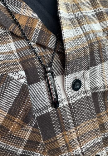 Close-up of a customer wearing their inscribed Black Bullet Urn Pendant against a brown plaid shirt.