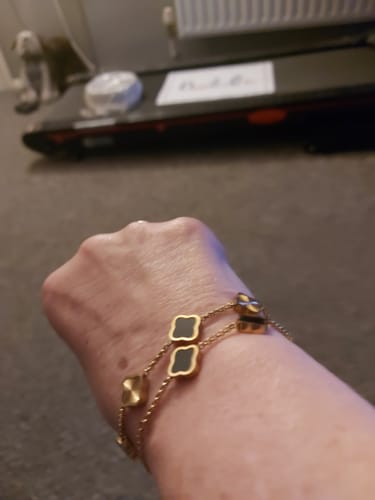 Close-up of a reviewer wearing the Celine Clover Bracelet, showing the black enamel and textured gold charms.