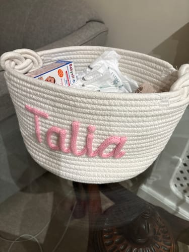 Customer's white personalized knitted basket with the name 'Talia' in pink, filled with baby items.