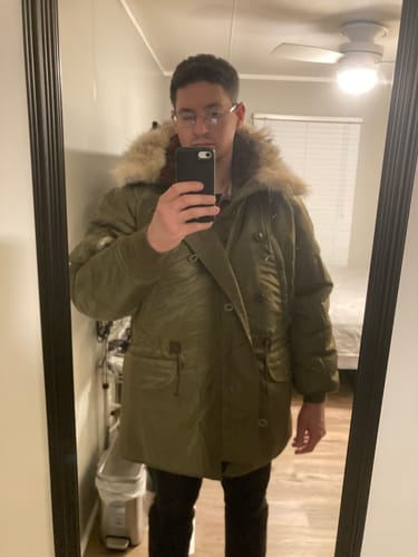 Reviewer in a mirror selfie wearing the closed, green 1945 Type N-3 Parka with its fur-lined hood.