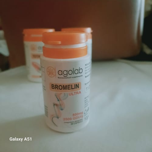 Recensore mostra un flacone di Bromelin ULTRA bianco con tappo arancione, con altri flaconi sullo sfondo.