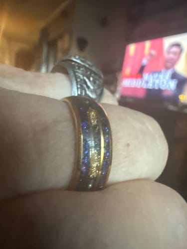 Close-up of a customer wearing the Ordanis ring, showing the gold band with a shimmering blue and purple opal inlay.