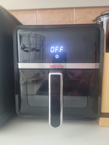 Recenzentul arată friteuza neagră Air Fryer Novio StonePro pe un blat, cu ecranul digital afișând 'OFF'.