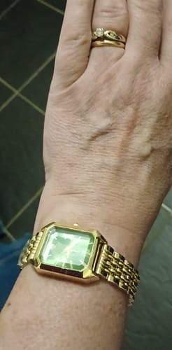 A customer wearing the CLAIRE DE MAINS watch with a green face and a gold-colored band.
