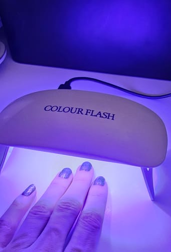 Ein Kunde benutzt die UV-LED-Lampe, um seine Nägel mit glitzerndem Lack unter dem violetten Licht zu trocknen.