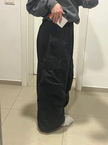 Customer's side view of the black baggy snow pants, showing the loose fit and a cargo pocket.