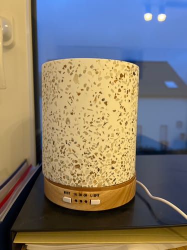 Rezensent zeigt den Living Green Aroma Diffuser mit Terrazzo-Optik und Holzsockel auf einem schwarzen Tisch.