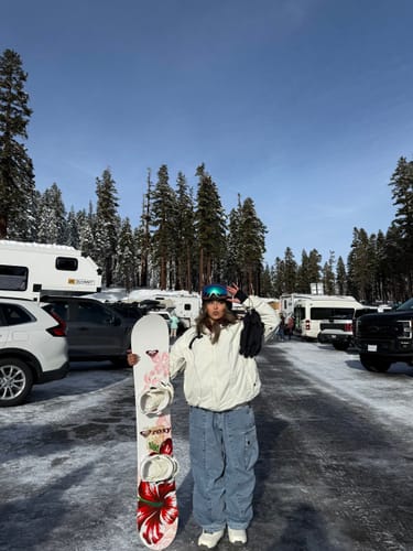 Reviewer in a snowy parking lot, wearing the Off White Snow Jacket while holding a snowboard.