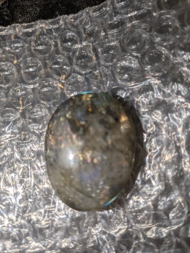 Close-up of reviewer's iridescent oval crystal with gold flecks, shown on bubble wrap.