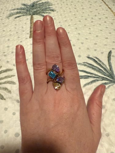 Customer's hand showing two Navae Birthstone Rings stacked, with blue, purple, and yellow stones.
