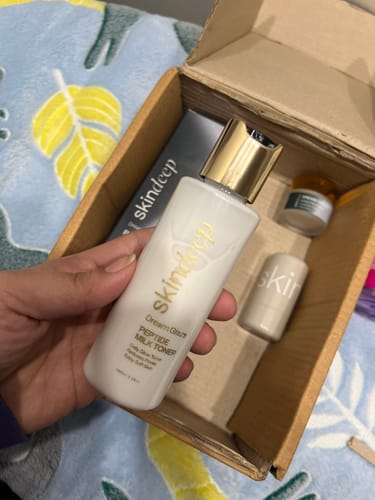 Customer holding the white bottle of DREAM GLAZE Peptide Milk Toner over an open shipping box.