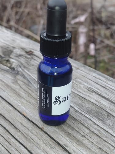Reviewer's Hair and Body Oil in a blue dropper bottle sitting on a weathered wooden surface.