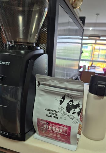 Reviewer's white pouch of Ethiopia ORO™ Yeast Fermentation coffee on a counter next to a black coffee grinder.