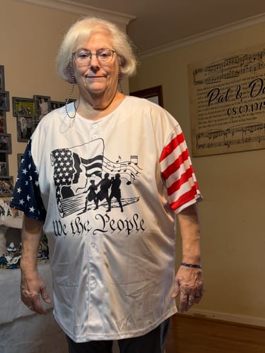 A reviewer wears the custom American flag baseball jersey, showing the 'We the People' graphic and flag-print sleeves.
