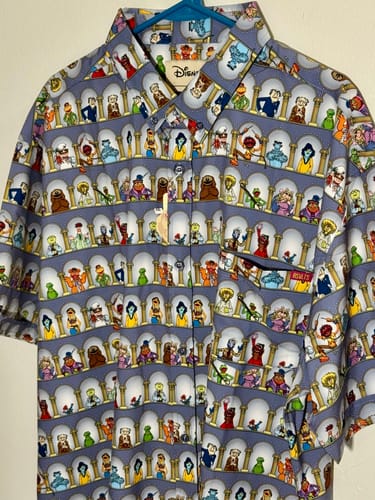 Reviewer's 'Light the Lights' Muppets shirt on a hanger, displaying its all-over pattern of characters in arches.