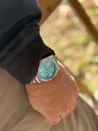 Customer wearing the Lucky Fours® Santos watch with a turquoise face and silver band outdoors.