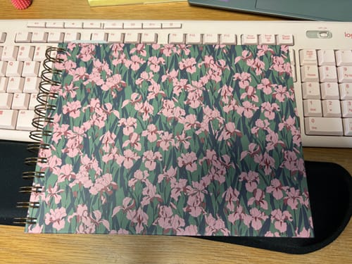 Customer's Anne Planner with the floral Pemberly Gardens cover, sitting closed on a desk in front of a keyboard.
