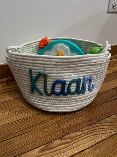 Customer's white knitted basket personalized with the name 'Kiaan' in multicolor yarn, holding toys.