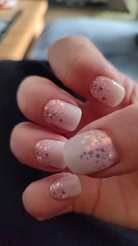 Hand einer Kundin, die die aufgetragenen 'Babyboomer Princess' UV Gel Nagelfolien mit Glitzer zeigt.