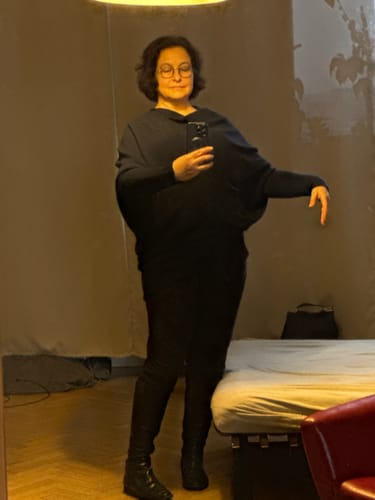 Customer demonstrating the draped sleeve of the navy Asymmetric Draped knit top in a mirror.