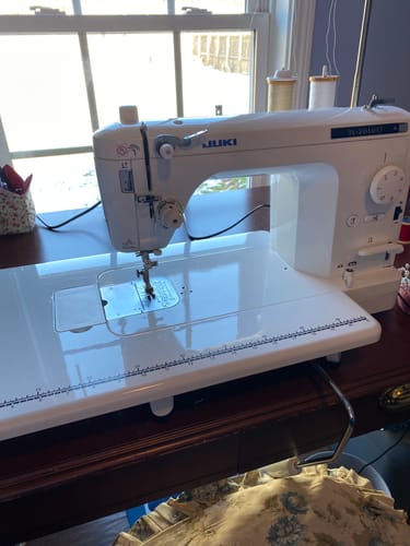 Reviewer's Juki TL-2010Q Quilting Machine with the large auxiliary table attached, set up on a wooden desk.