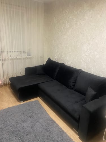 Kliento juoda kampinė sofa, stovinti svetainėje ant šviesių medinių grindų.