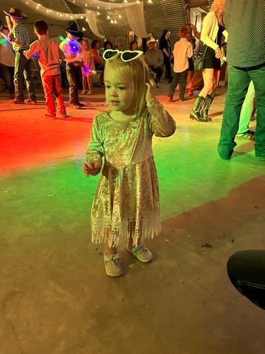Reviewer's daughter standing in a shiny, fringed dress at a party with colorful lights.