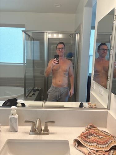 Reviewer's mirror selfie showing a natural-looking tan on their torso after using Bro Glo Foam Body Tanner.