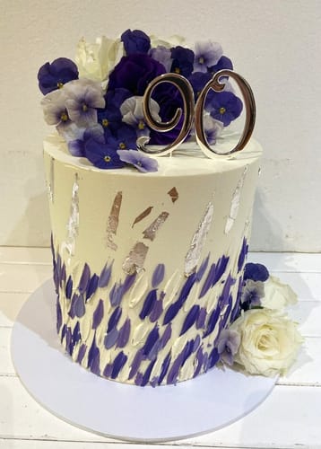 Customer's white birthday cake topped with purple Royal Blue Violas and a '90' cake topper.