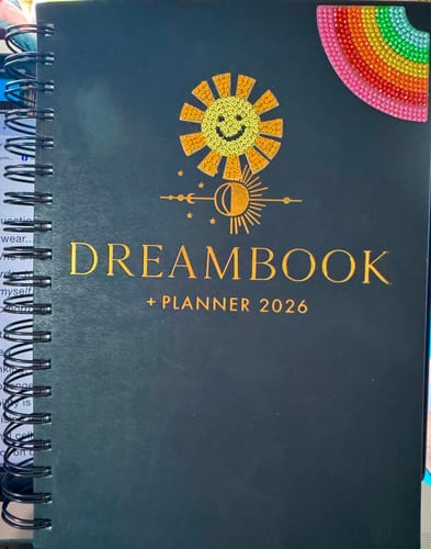 Reviewer's black 2026 Dreambook + Planner, customized with sparkly sun and rainbow stickers on the cover.