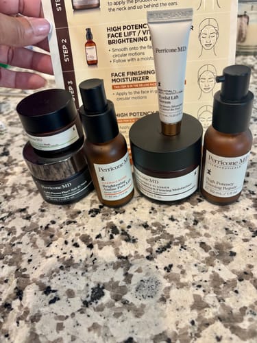 Customer's Neck & Face Firming Kit products, including amber bottles and black jars, displayed on a granite countertop.