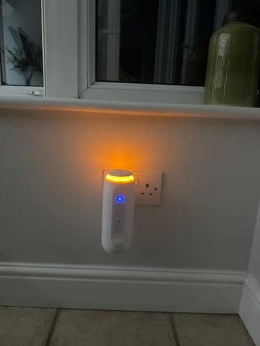 Customer's plug-in diffuser for the Rain-Kissed Garden fragrance, glowing with a warm orange light in a wall socket.