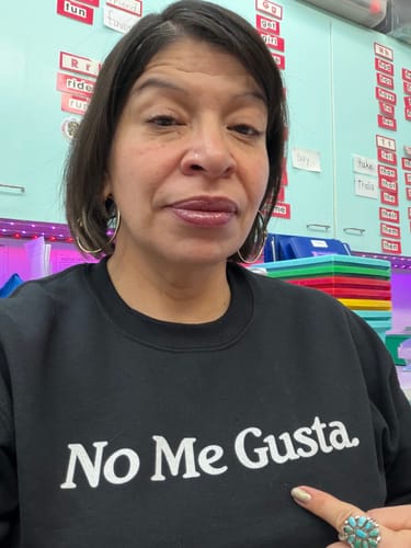 Reviewer in a classroom pointing to the white text on her black No Me Gusta OG Sweatshirt.
