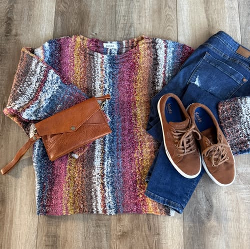 Customer's striped boat neck sweater styled in a flat lay with jeans, brown sneakers, and a wristlet.