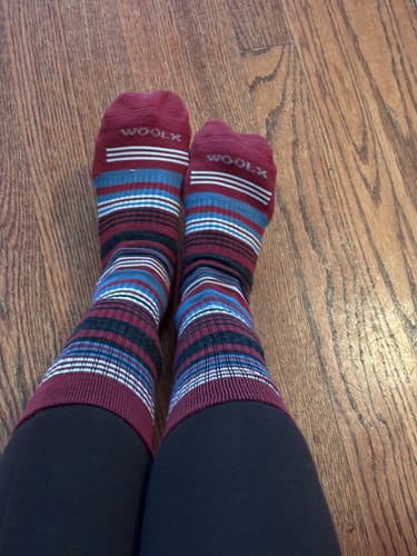 Customer wearing the striped Everyday Crew Socks, showing the fit on their legs while seated on a wood floor.