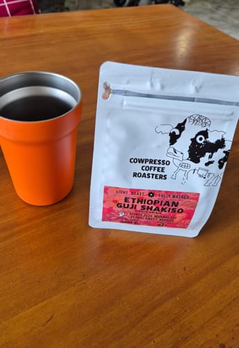 Customer's bag of Ethiopian Guji Shakiso coffee next to an orange mug on a wooden table.