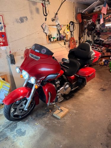 Customer's red motorcycle with the black Wind Rider Seat Cover installed, viewed from the front in a garage.