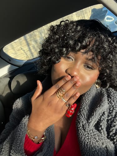 Customer taking a selfie in a car, showing the gold Celine Clover Bracelet with white charms on their wrist.