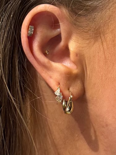 Customer's ear showing the gold Cluster huggies with clear stones in a second lobe piercing, styled with other jewelry.
