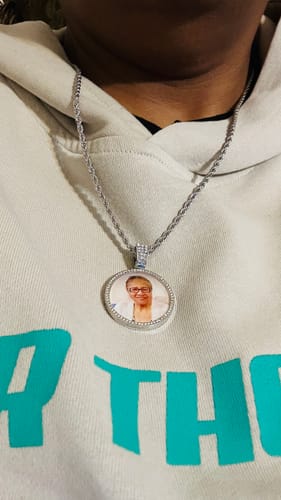 Close-up of a reviewer wearing the round, diamond-studded photo necklace against a light-colored hoodie.