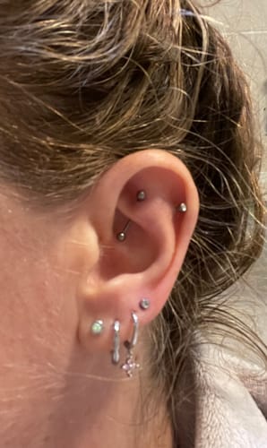 Close-up of a reviewer's ear wearing the pink crystal Lucky Charm huggie earring among several other silver earrings.