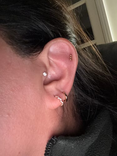 Reviewer showing the Solitaire flatback Gold stud in their tragus piercing among other earrings.