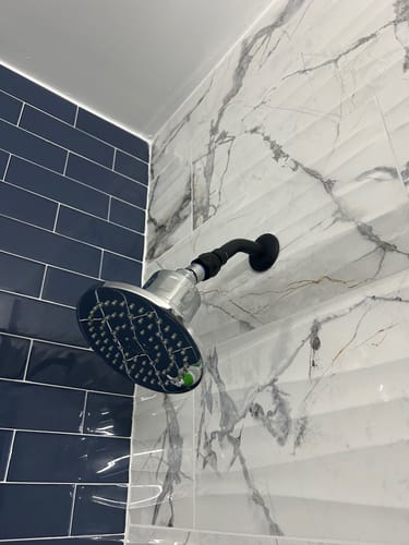 Customer's Gillian filtered shower head installed on a wall with white marble-patterned tile.