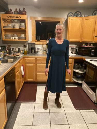Reviewer wearing the blue Caroline Ribbed Twirl Dress with brown boots while standing in a kitchen.