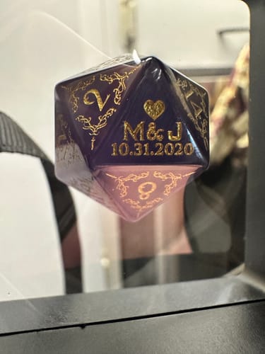 Customer's close-up of the personalized purple D20 dice showing the engraving 'M&J 10.31.2020' in gold.