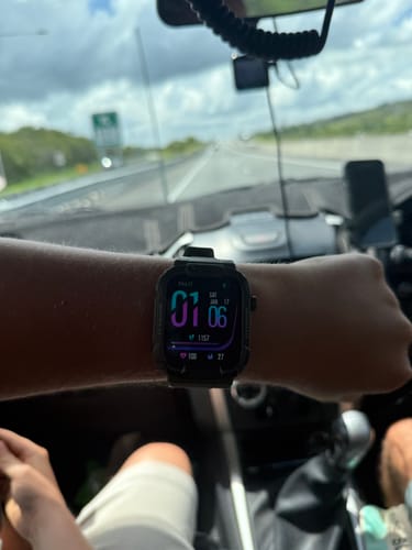 A customer's black digital watch with a colorful display, shown on their wrist inside a car.