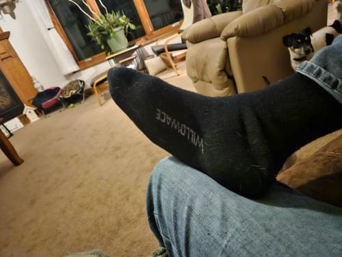 Close-up of a reviewer's foot in a black Men's Alpaca Sock, relaxing in a living room.