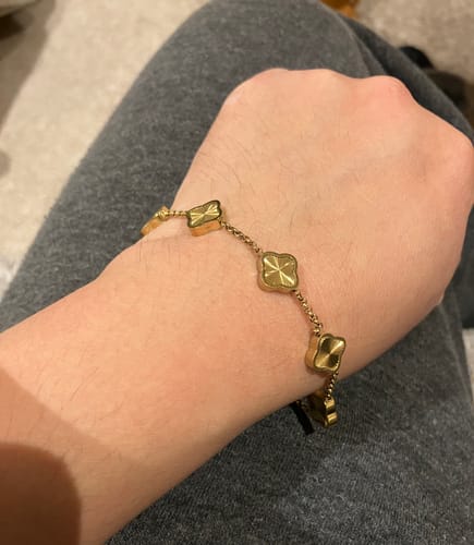 Customer wearing a gold chain bracelet with clover-shaped charms on their wrist.