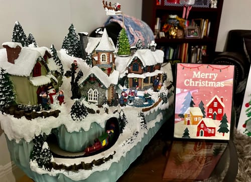 Customer's finished mini Christmas painting of snowy houses displayed next to a ceramic village.