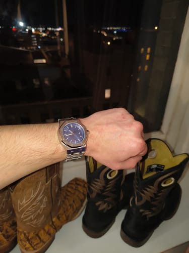 Customer wearing their silver Lucky Fours Oceanus watch with a blue dial on their wrist in front of a window at night.